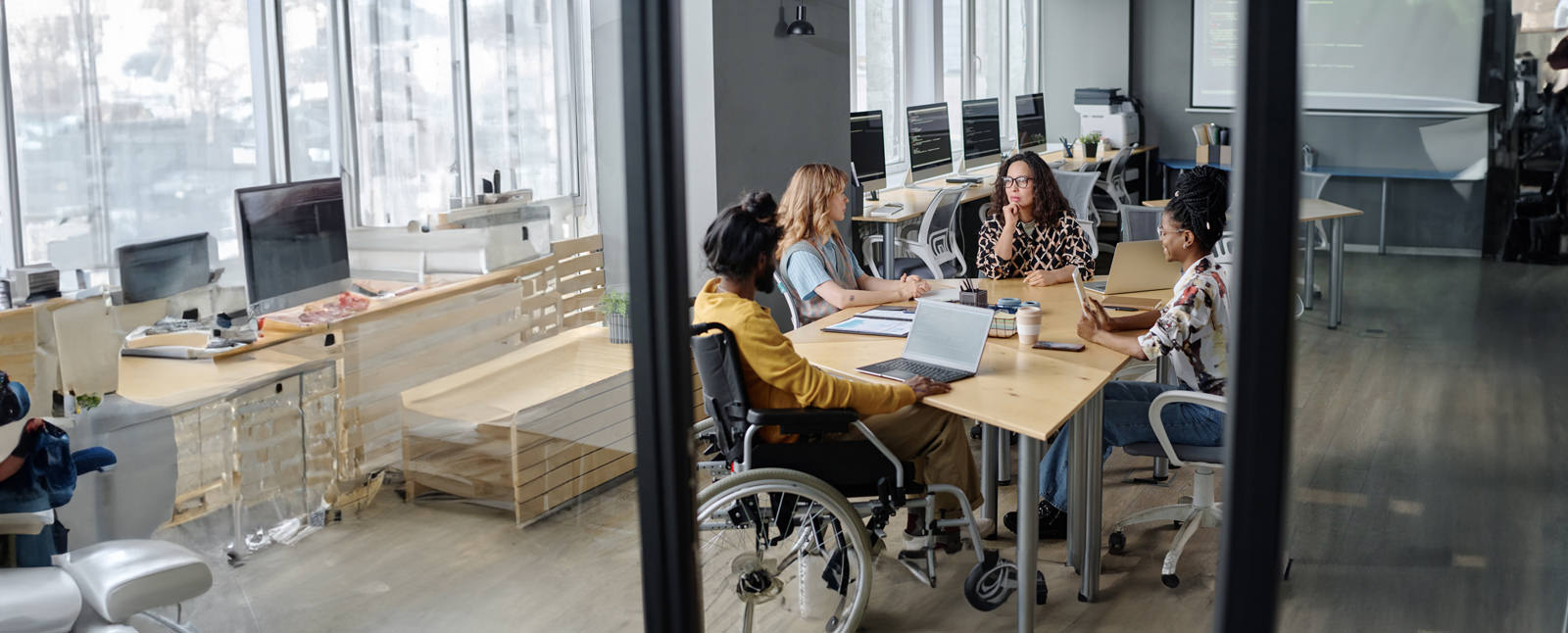 A group meeting in a computer tech office at a round table with one member in a wheel-chair