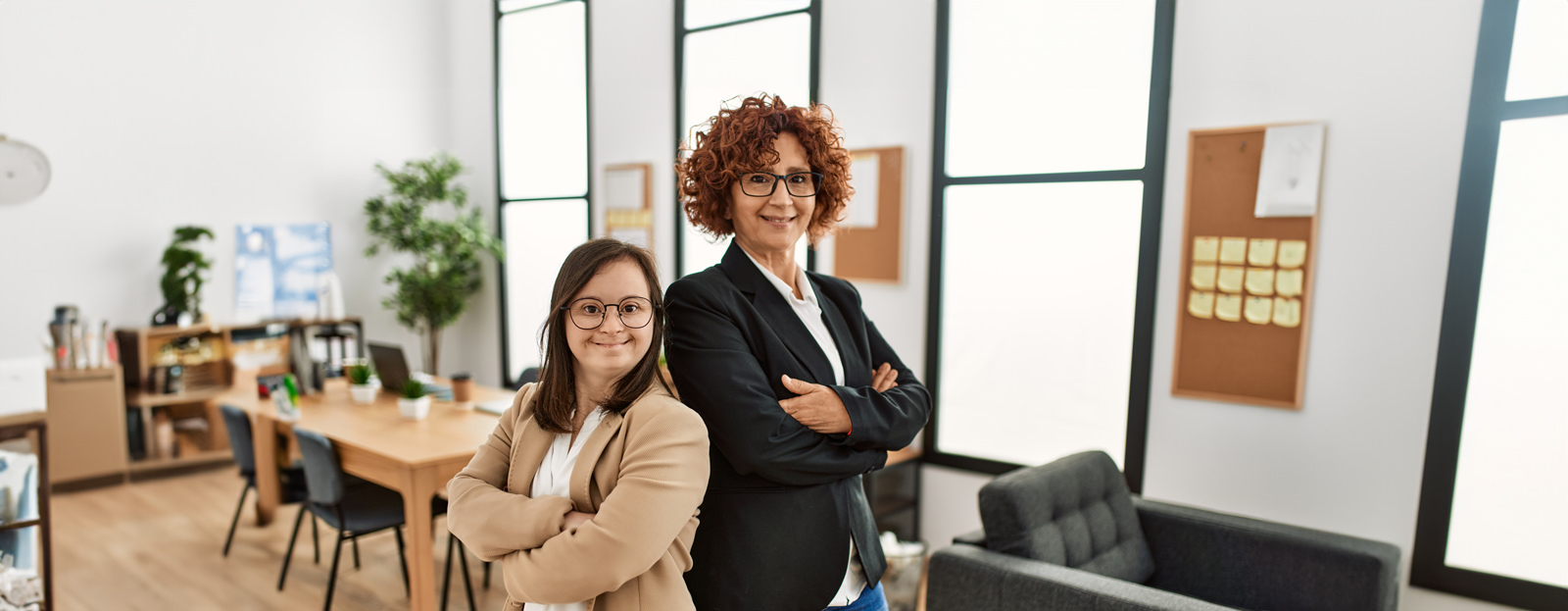 Two woman standing back to back in an office smiling at camera